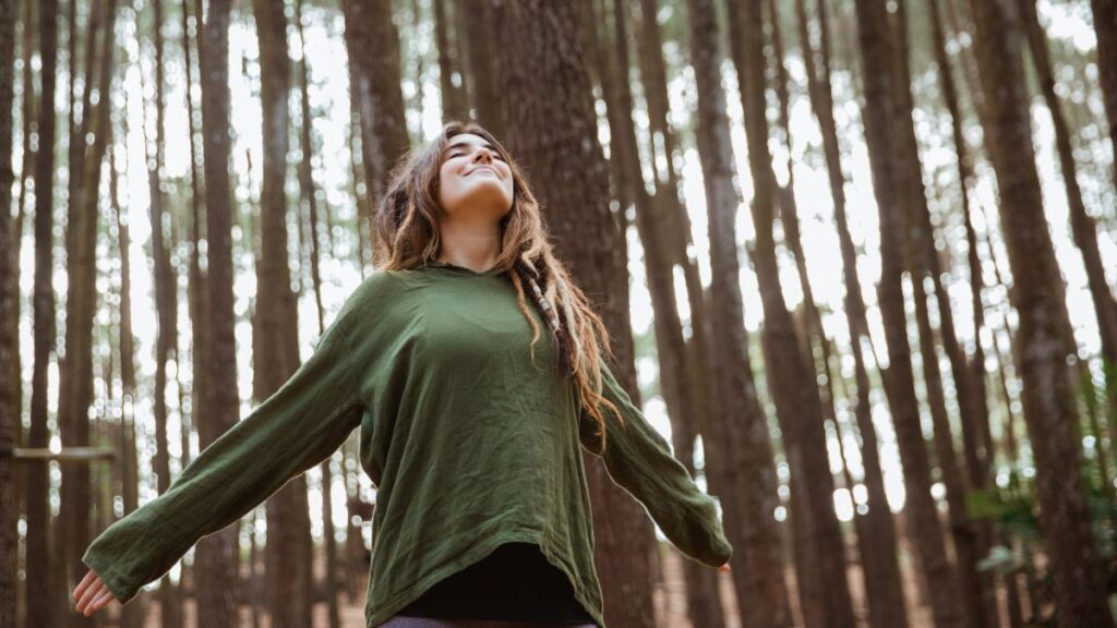 Eine Frau die Tief einatmet mit ausgestreckten Armen im Wald