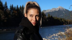 Mara steht im Herbst an einem Fluss und schaut in die Sonne